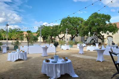 Groupe de personnes rassemblées dans une cour extérieure arborée avec des tables dressées pour un événement.