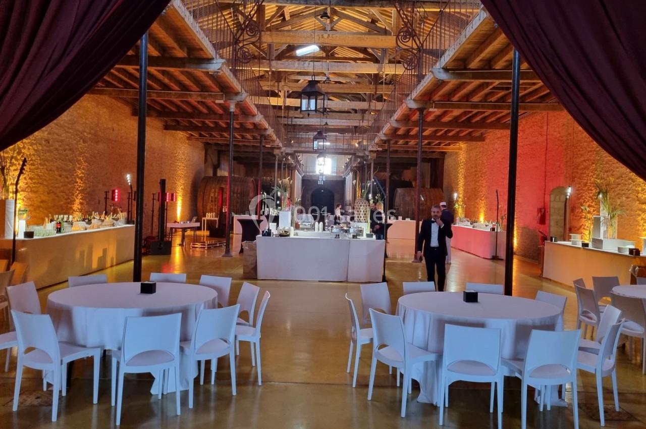 Salle de réception avec tables rondes dressées, éclairage chaleureux et buffets alignés le long des murs en pierre.