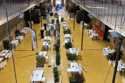 Groupe de personnes rassemblées dans une cour extérieure arborée avec des tables dressées pour un événement.