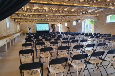 Groupe de personnes rassemblées dans une cour extérieure arborée avec des tables dressées pour un événement.