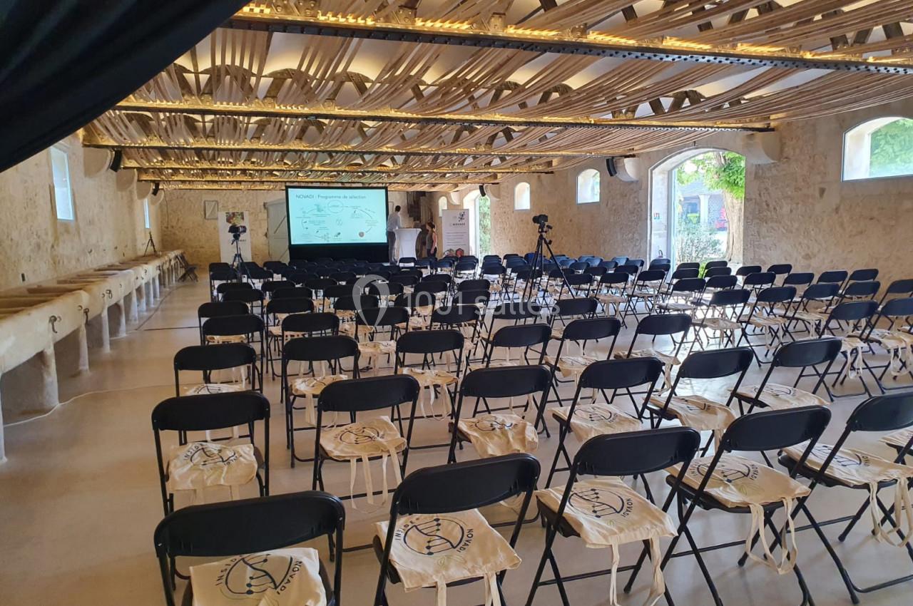 Salle de conférence lumineuse avec des rangées de chaises noires, sacs en tissu posés dessus, et un écran de présentation au…