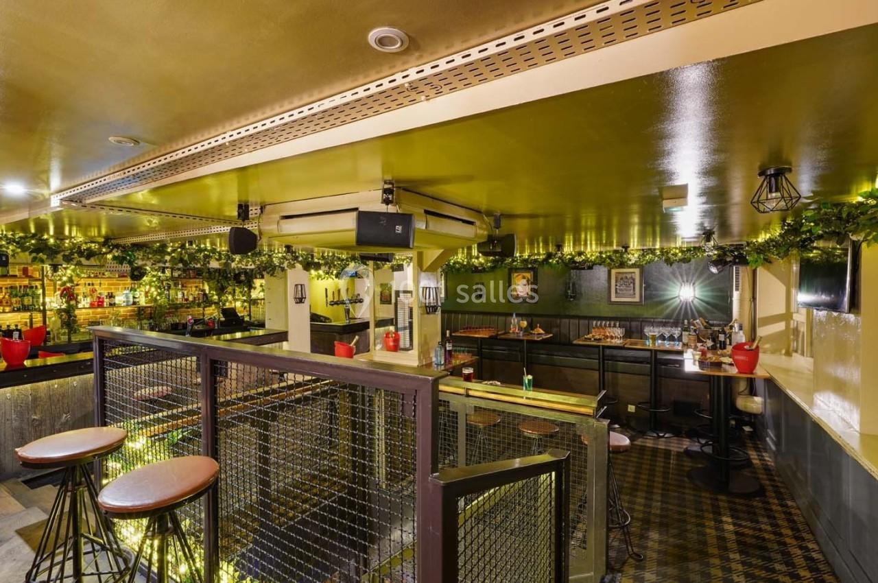 Intérieur d'un bar chaleureux avec des tables hautes, des décorations végétales et un éclairage tamisé.