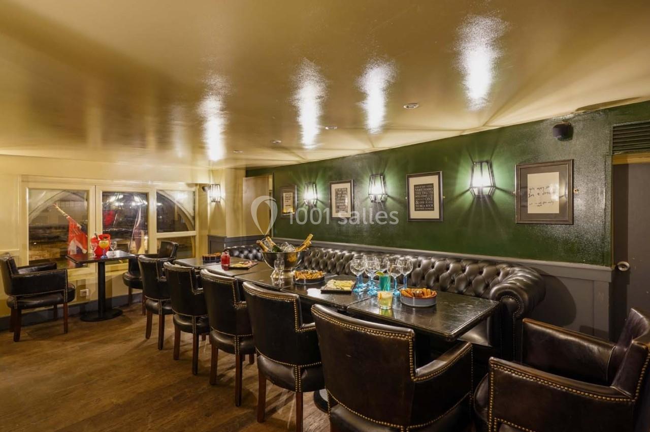 Salle élégante avec table en bois, chaises en cuir, murs verts, éclairage tamisé et vue sur l'extérieur.