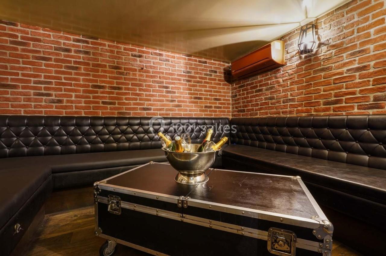 Salle avec murs en briques, banquettes en cuir noir, table basse en métal et seau rempli de bouteilles de champagne.