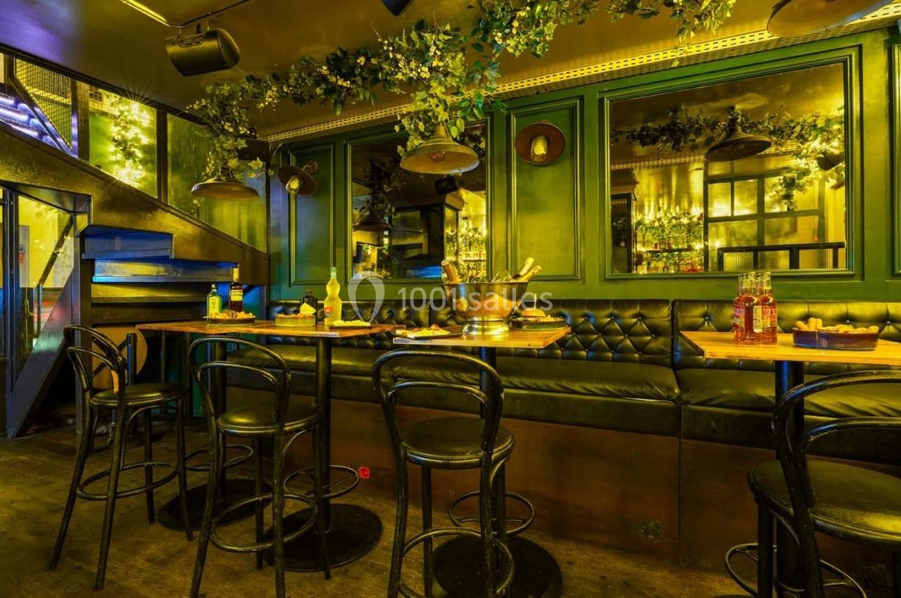 Salle de restaurant avec banquettes noires, tables en bois, chaises sombres et décorations végétales suspendues.