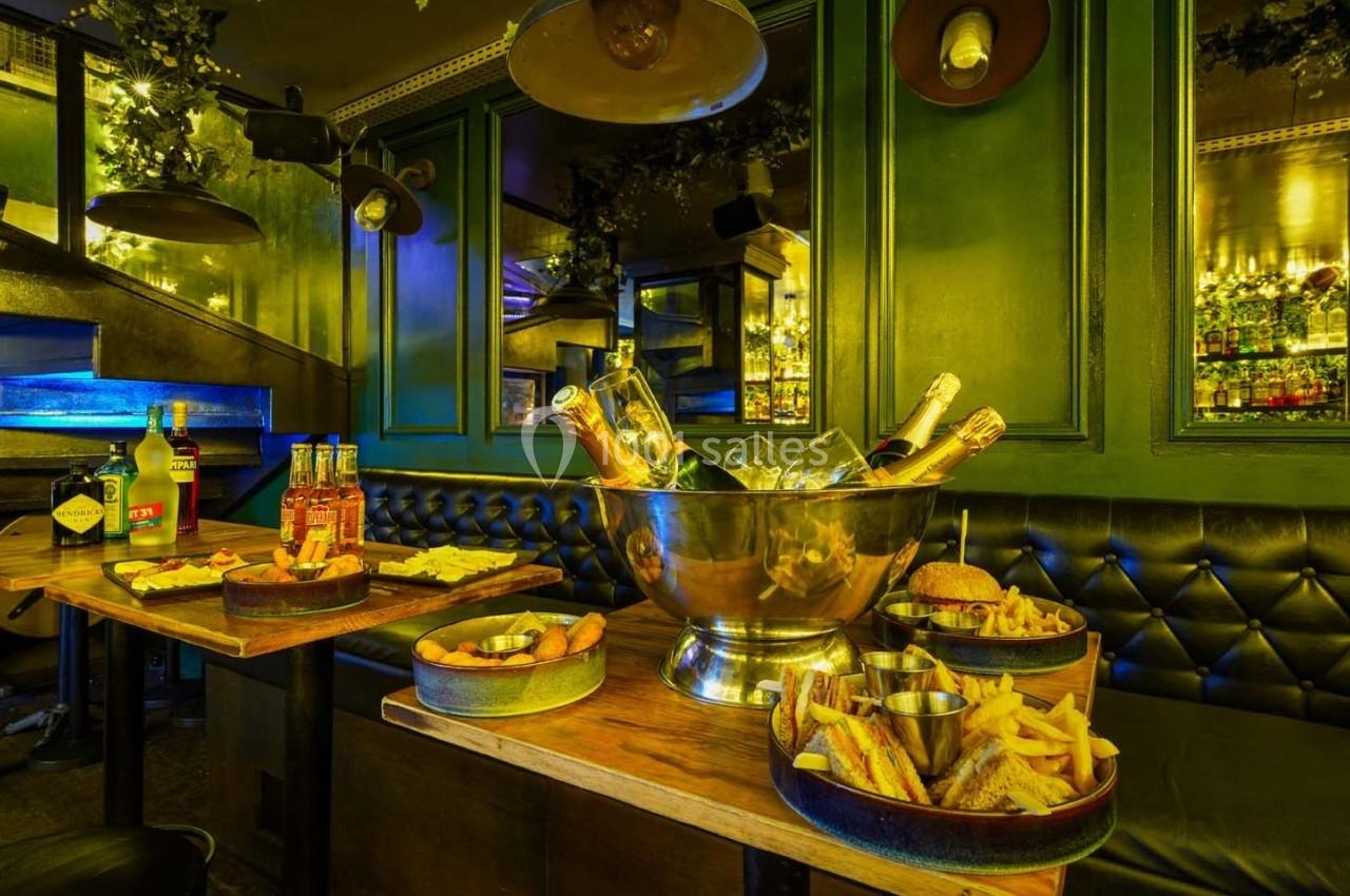 Table garnie de plats variés, bouteilles de champagne dans un seau à glace, décor intérieur avec banquettes et éclairage…