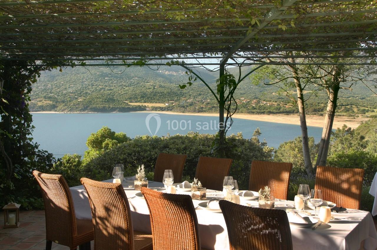 Table dressée sous une pergola ombragée avec vue sur un lac entouré de collines verdoyantes.