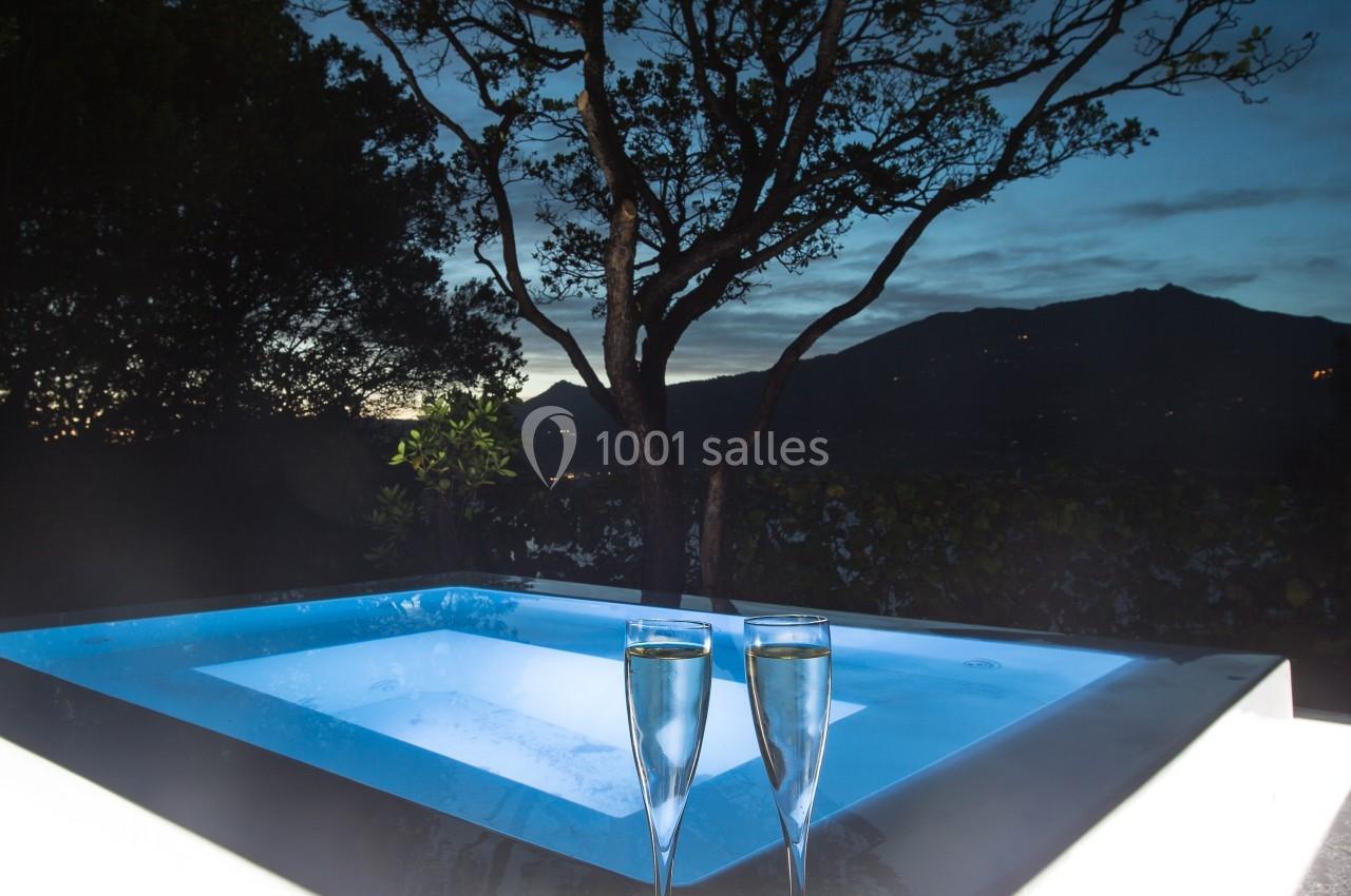 Bain à remous éclairé en extérieur, entouré d'arbres, avec deux verres de champagne au premier plan.