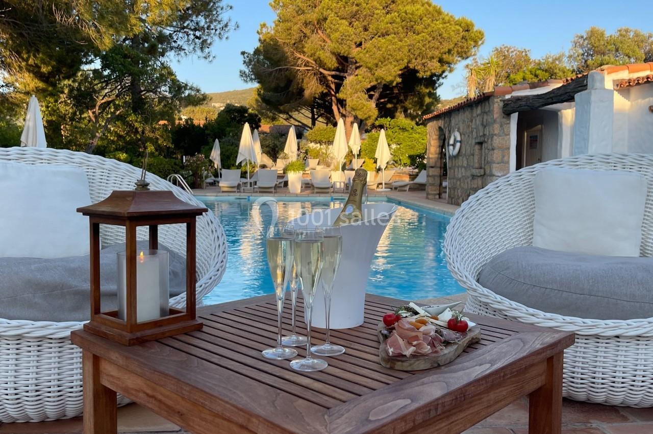 Deux fauteuils en rotin, une table avec des verres de champagne et des amuse-bouches, près d'une piscine entourée de…