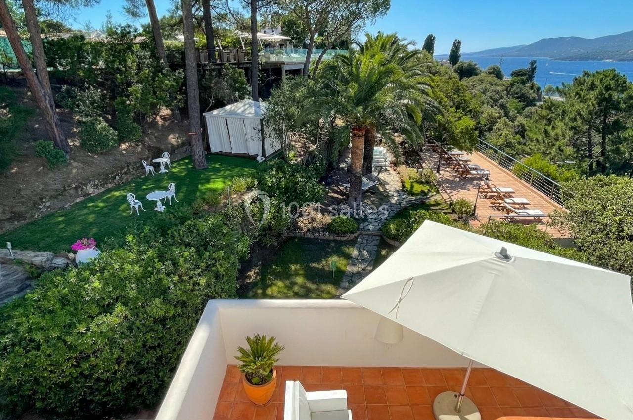 Vue depuis une terrasse sur un jardin verdoyant avec mobilier extérieur, une pergola et un panorama sur la mer.
