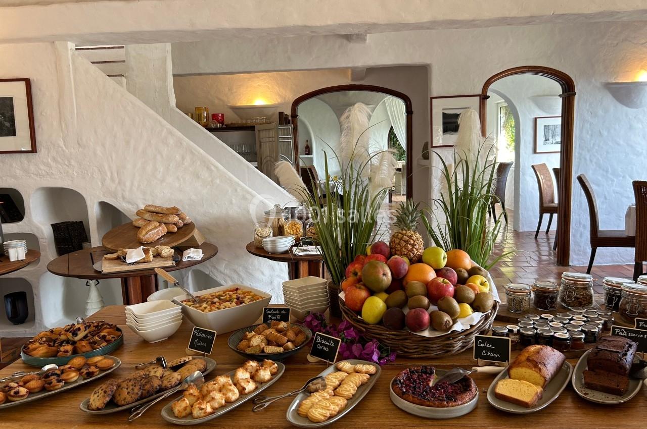 Buffet de petit-déjeuner avec fruits frais, viennoiseries, pains, confitures et plats variés dans une salle lumineuse.