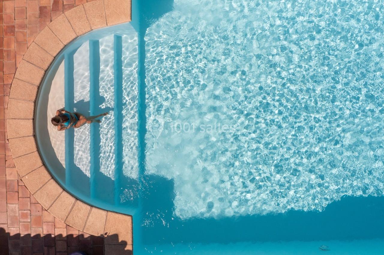 Vue aérienne d'une femme descendant des marches dans une piscine entourée de dalles en terre cuite.