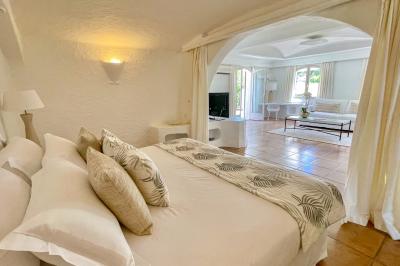 Salon lumineux avec canapé blanc, table basse, bureau près de la fenêtre et vue sur un jardin verdoyant.