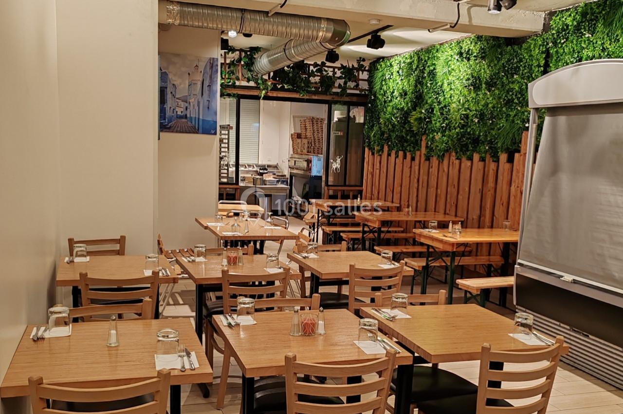 Salle de restaurant lumineuse avec tables en bois, chaises assorties et mur végétalisé en arrière-plan.