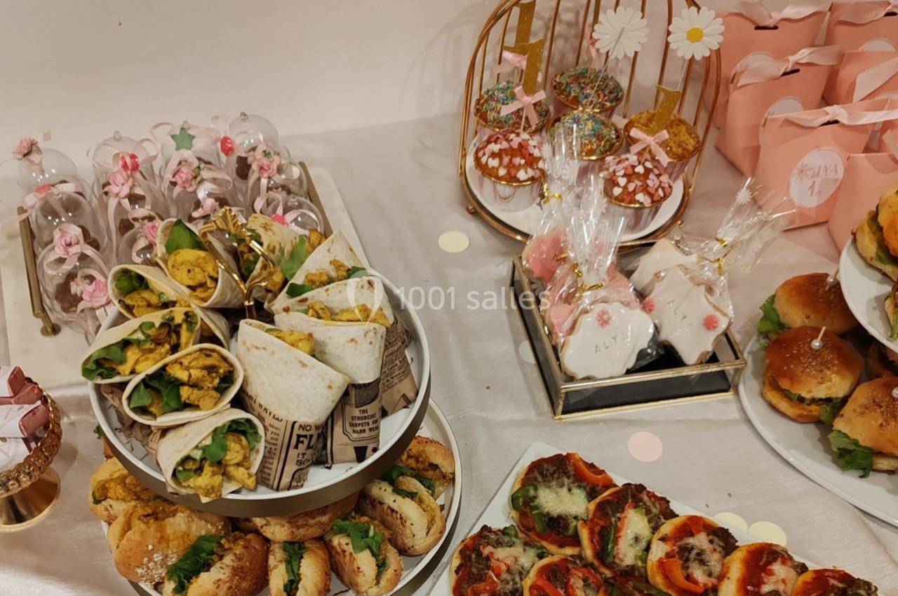 Table garnie d'un buffet comprenant wraps, mini-burgers, pizzas, pâtisseries et décorations festives.
