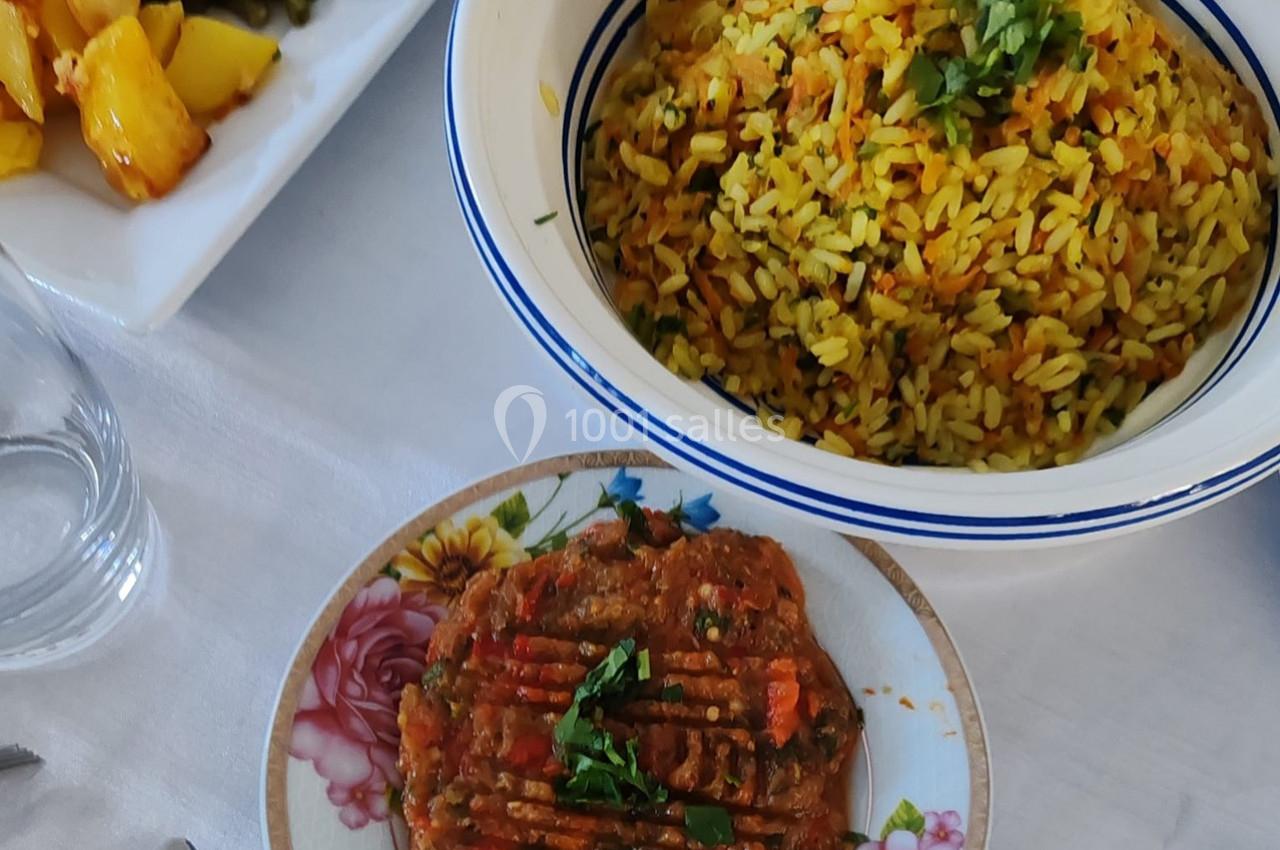 Assiette de riz jaune garni d'herbes fraîches, accompagnée d'un plat de légumes mijotés et d'une garniture colorée.