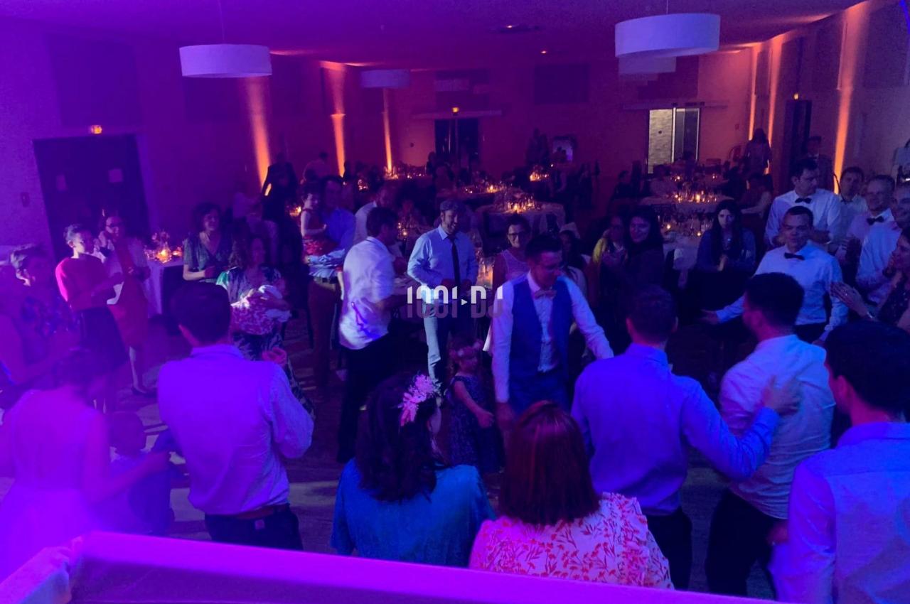 Des personnes dansent dans une salle éclairée par des lumières colorées lors d'un événement festif en soirée.