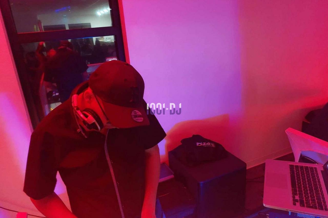 Un DJ portant une casquette mixe de la musique sur une console dans une ambiance lumineuse rouge et violette.