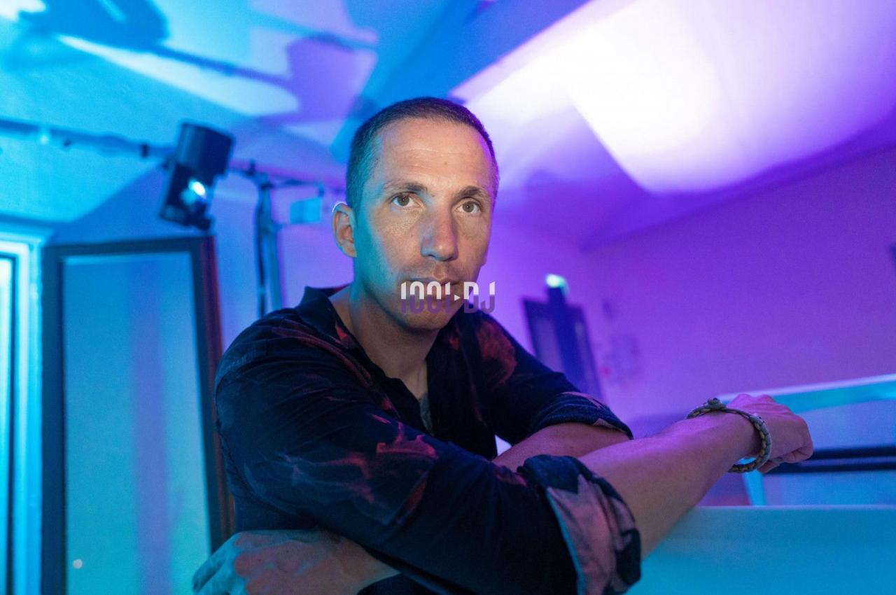 Homme appuyé sur une surface dans une pièce éclairée de lumières bleues et violettes.