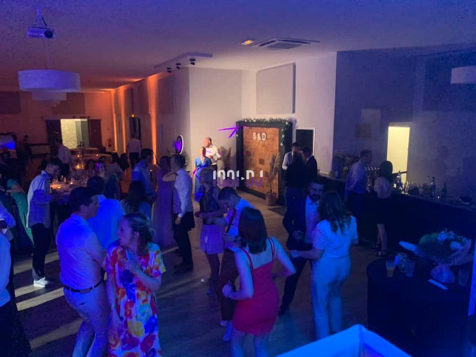 Personnes dansant et discutant dans une salle éclairée par des lumières colorées, ambiance festive en soirée.