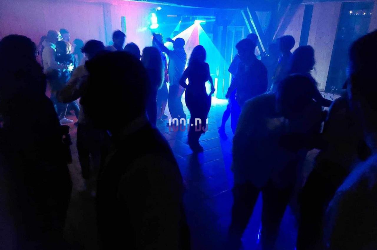 Personnes dansant dans une salle sombre éclairée par des lumières colorées et un projecteur.