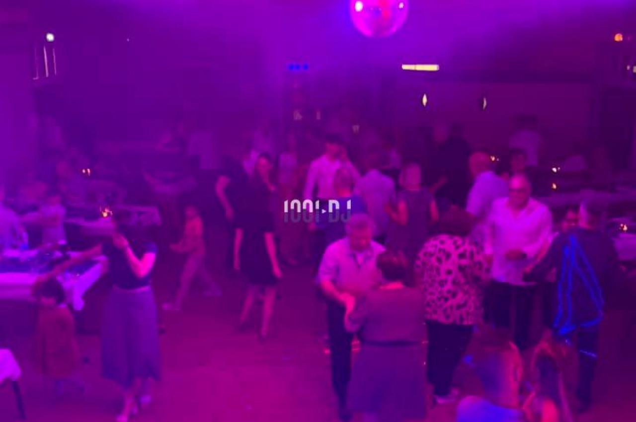 Des personnes dansent et discutent dans une salle éclairée par des lumières colorées, avec une boule disco au plafond.