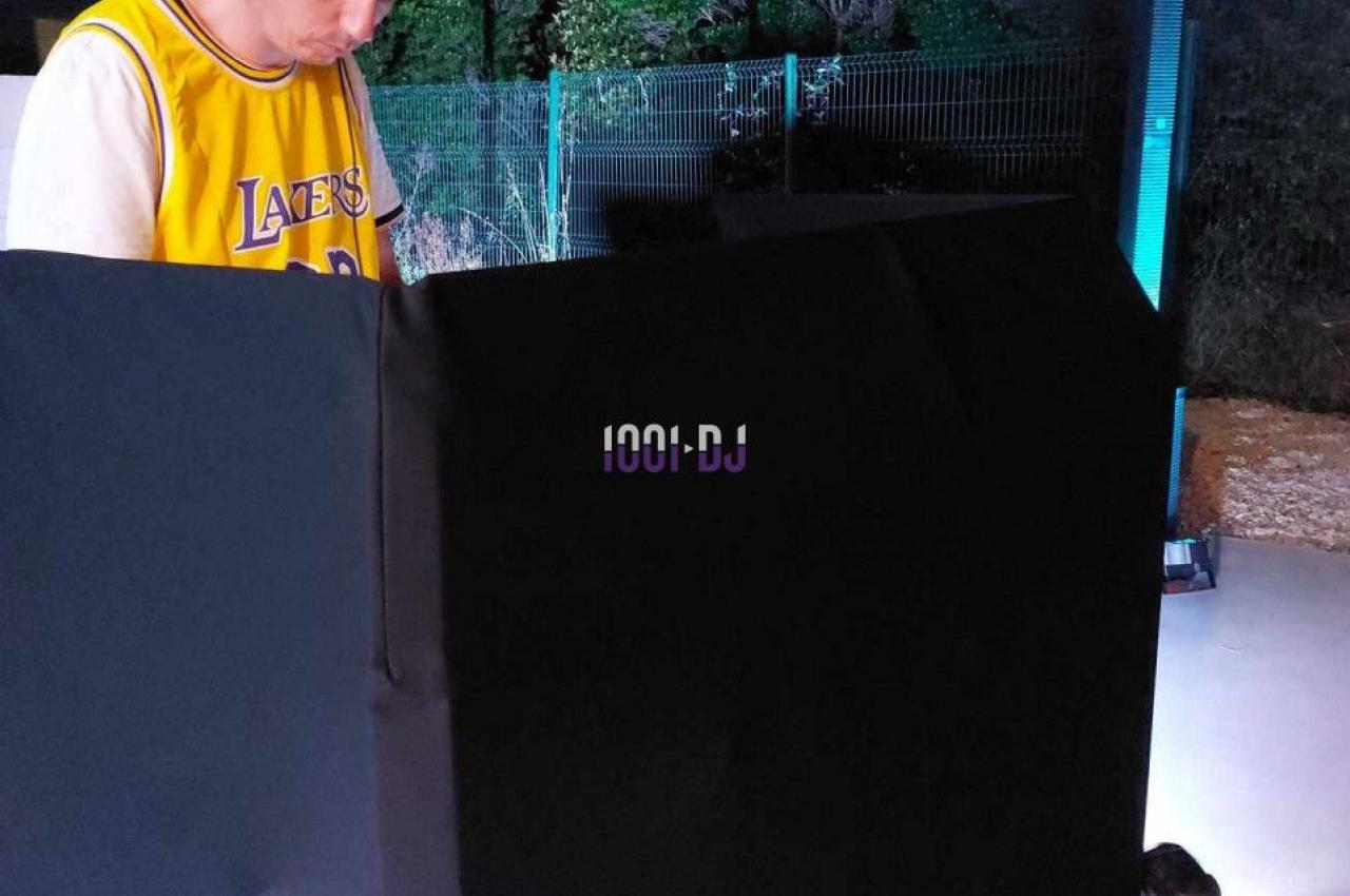 Un DJ portant un casque audio mixe de la musique en extérieur, devant un équipement éclairé dans la nuit.