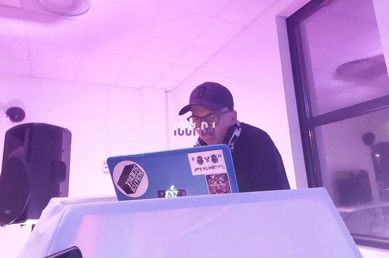 Un homme portant une casquette mixe de la musique sur un ordinateur portable dans une salle éclairée en rose.