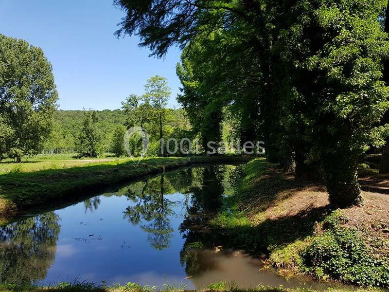 Vue d'un cours d'eau bordé d'arbres et de végétation sous un ciel bleu clair.