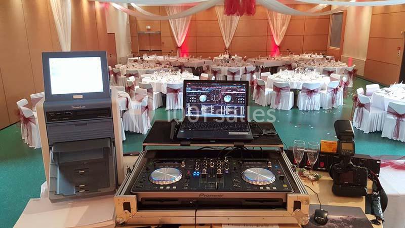 Vue d'une installation de DJ avec platines et ordinateur, face à une salle de réception décorée et dressée pour un événement.