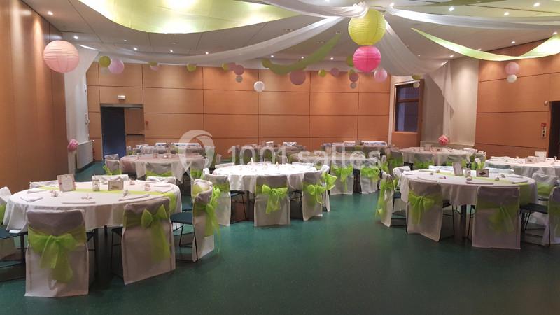 Salle de réception décorée avec des tables rondes, nappes blanches, nœuds verts et lanternes suspendues.