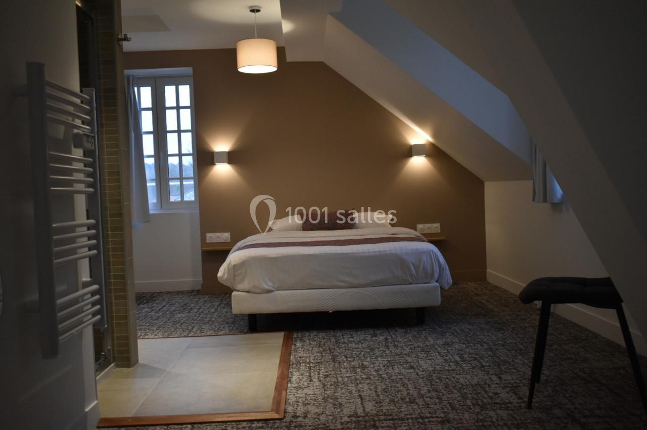 Chambre mansardée avec un lit double, éclairage mural, moquette au sol et salle de bain attenante visible à gauche.