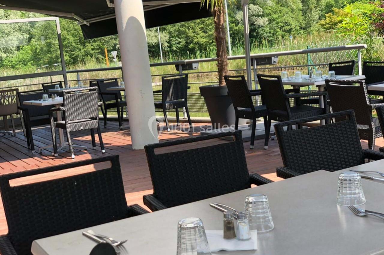 Terrasse extérieure avec tables dressées, chaises en osier noir, vue sur un espace verdoyant et végétation environnante.