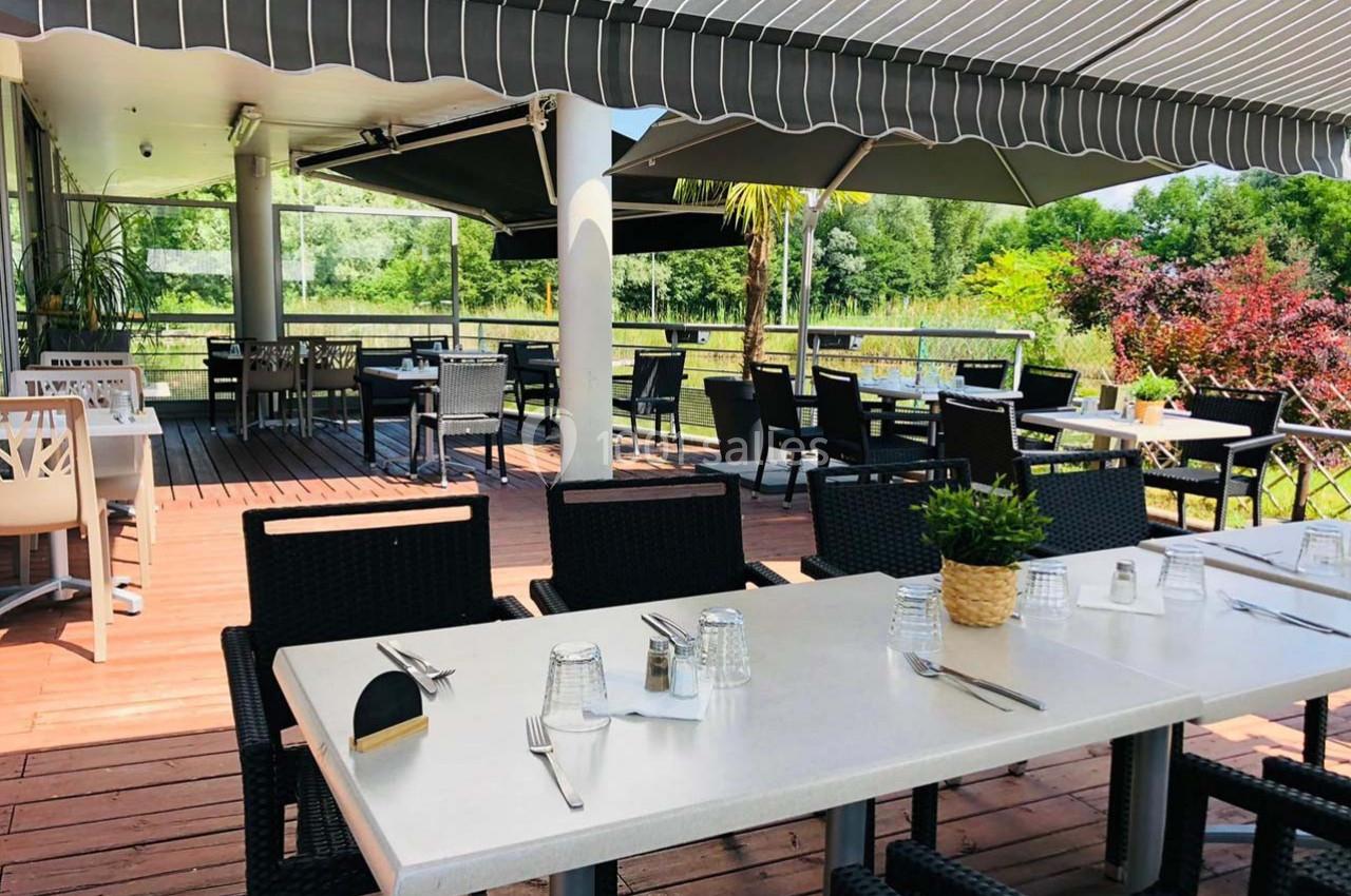 Terrasse extérieure d'un restaurant avec tables dressées, chaises en osier noir et vue sur un jardin verdoyant.