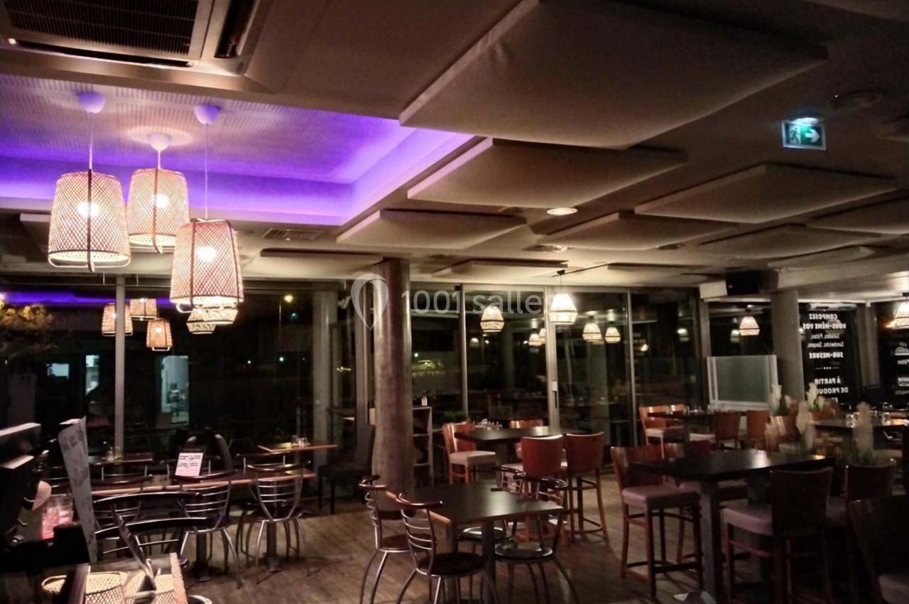 Salle de restaurant moderne avec éclairage tamisé, plafonniers suspendus et grandes baies vitrées donnant sur l'extérieur.