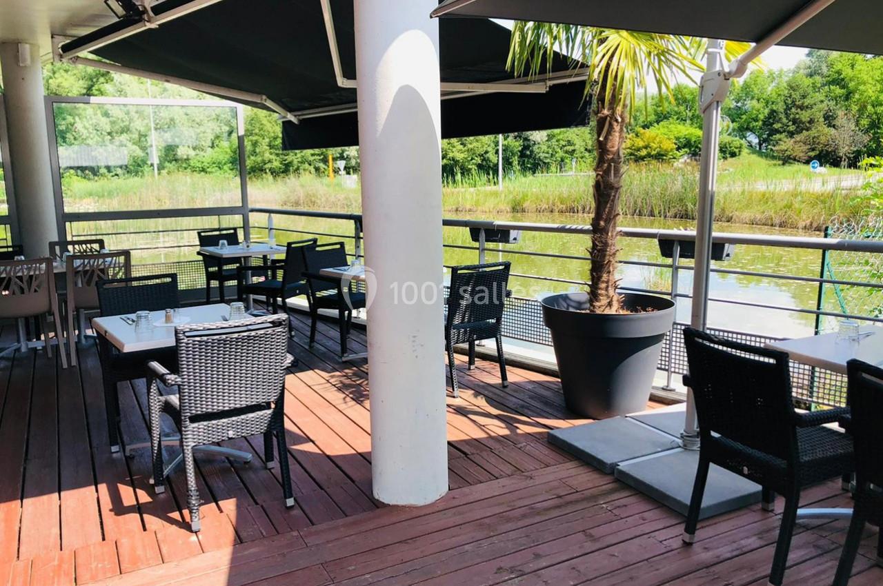 Terrasse en bois avec tables et chaises noires, ombragée par des parasols, donnant sur un paysage verdoyant avec un plan d…