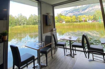 Étang entouré de végétation avec des montagnes en arrière-plan sous un ciel bleu parsemé de nuages.
