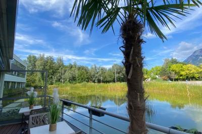 Étang entouré de végétation avec des montagnes en arrière-plan sous un ciel bleu parsemé de nuages.
