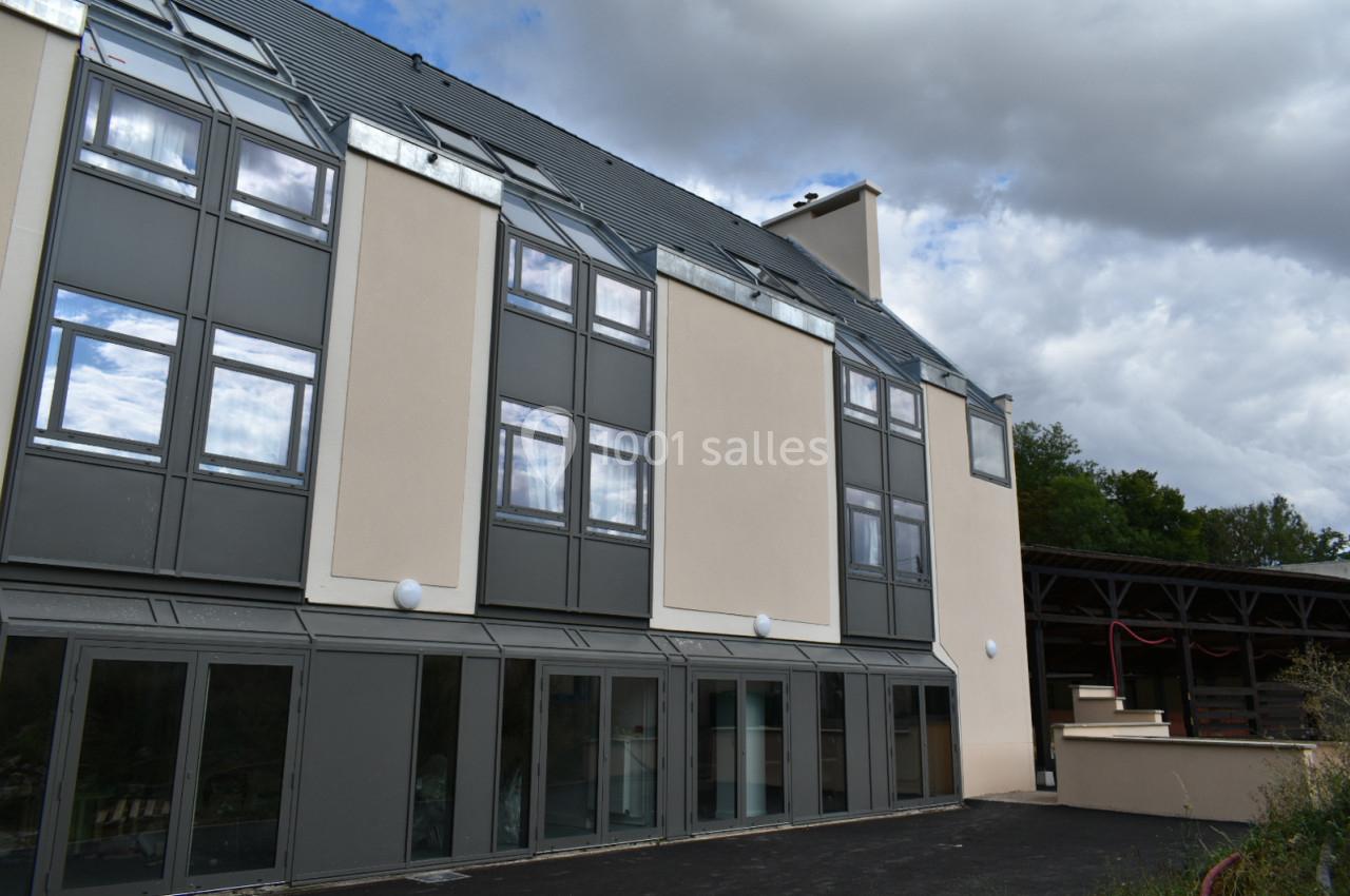 Façade d'un bâtiment moderne à plusieurs étages avec de grandes fenêtres et un toit incliné sous un ciel nuageux.