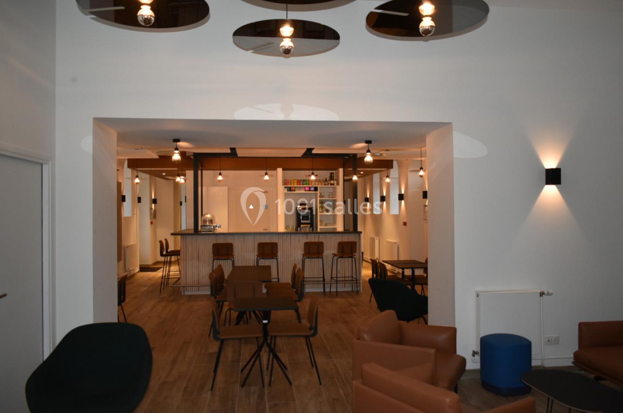 Espace intérieur moderne avec tables, chaises et un comptoir de bar éclairé par des suspensions.