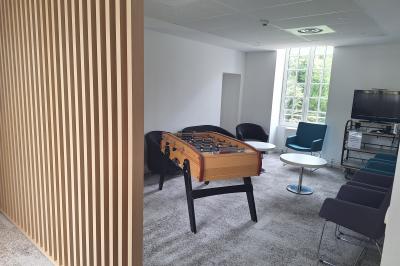 Bâtiment circulaire en pierre avec une pelouse et des arbres, sous un ciel partiellement nuageux.