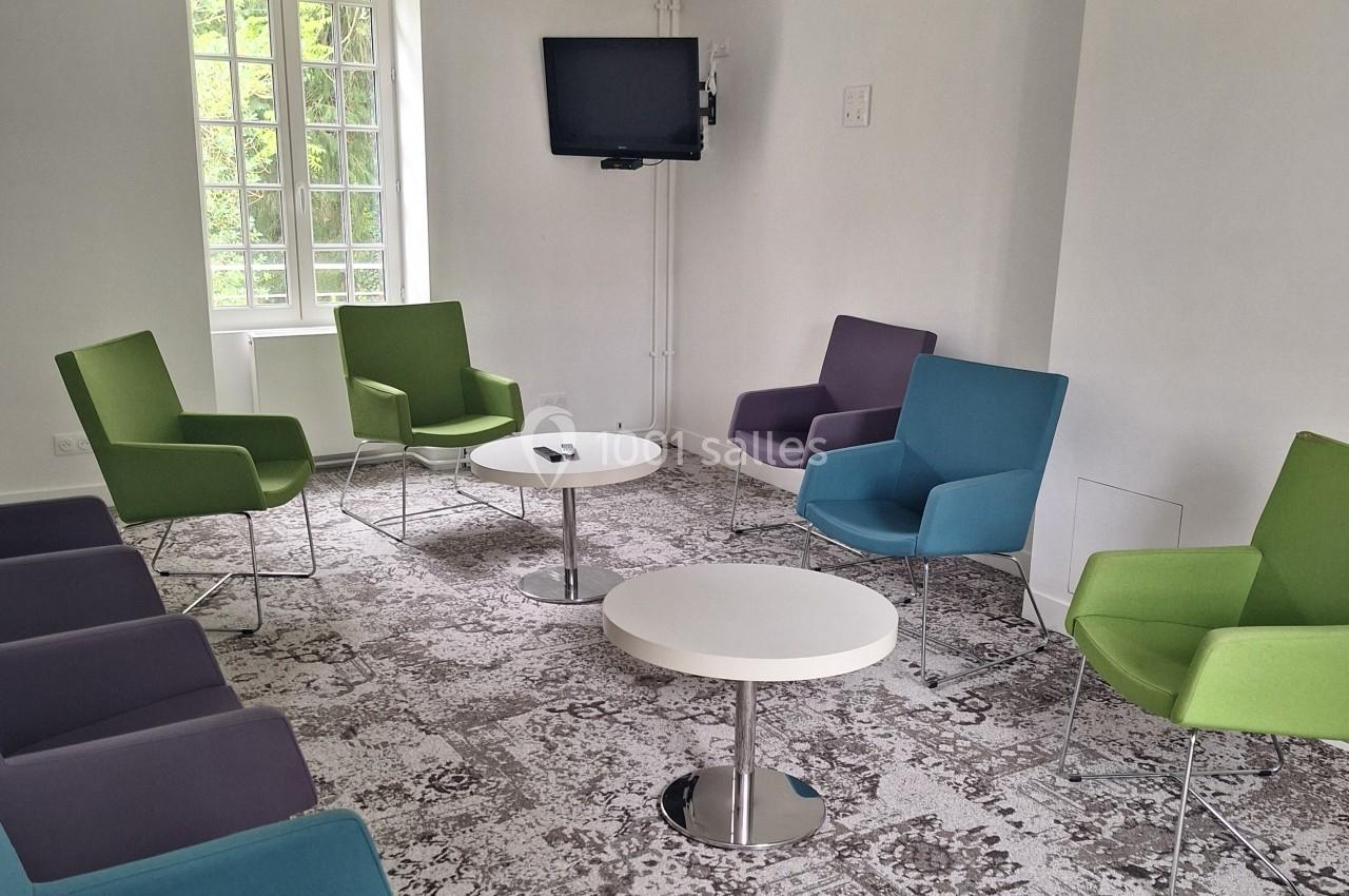 Salle lumineuse avec plusieurs fauteuils colorés disposés en cercle autour de petites tables basses blanches.