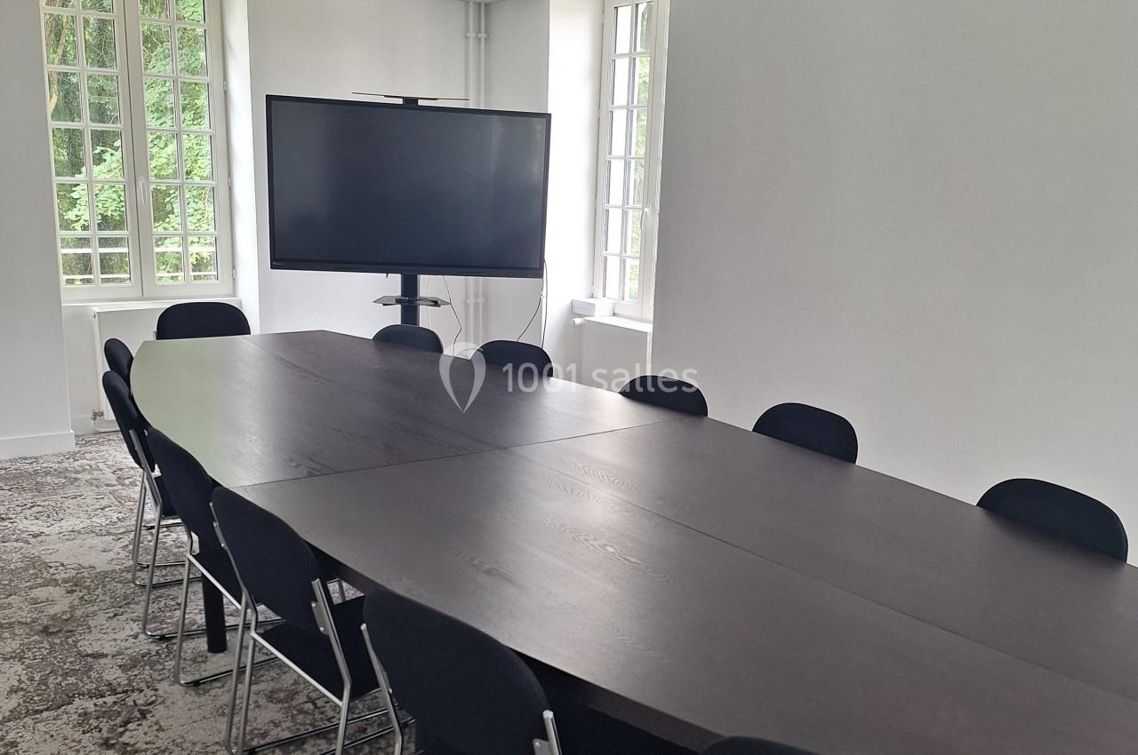 Salle de réunion lumineuse avec une grande table en bois foncé, des chaises noires et un écran sur pied.
