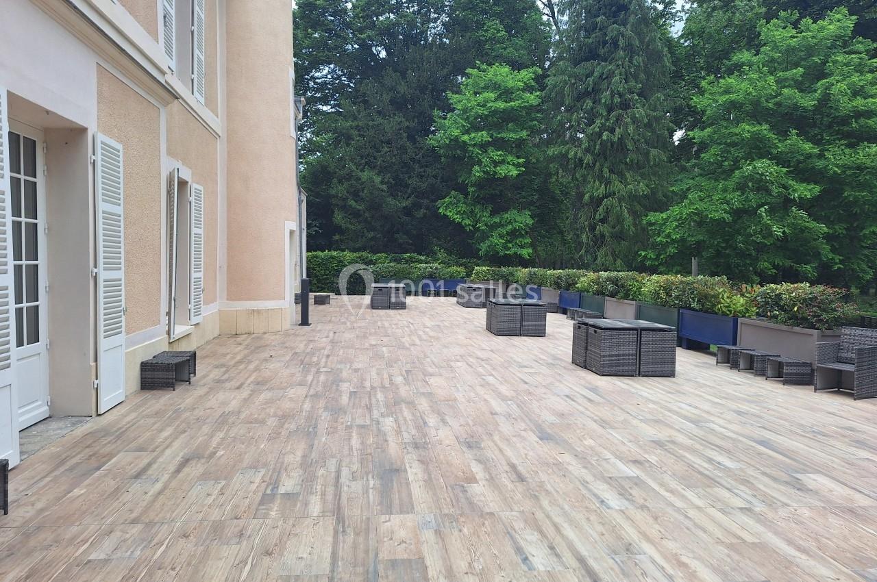 Terrasse en bois clair avec mobilier en rotin, bordée de jardinières et entourée de végétation dense.