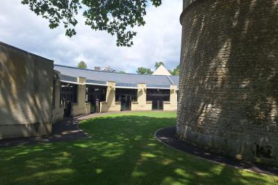 Bâtiment circulaire en pierre avec une pelouse et des arbres, sous un ciel partiellement nuageux.