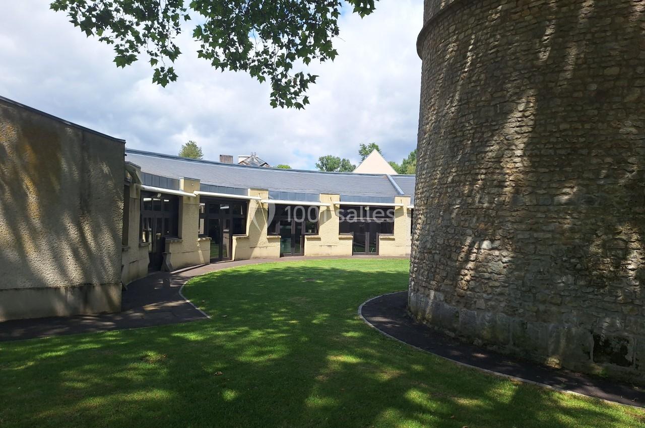 Bâtiment circulaire en pierre avec une pelouse et des arbres, sous un ciel partiellement nuageux.