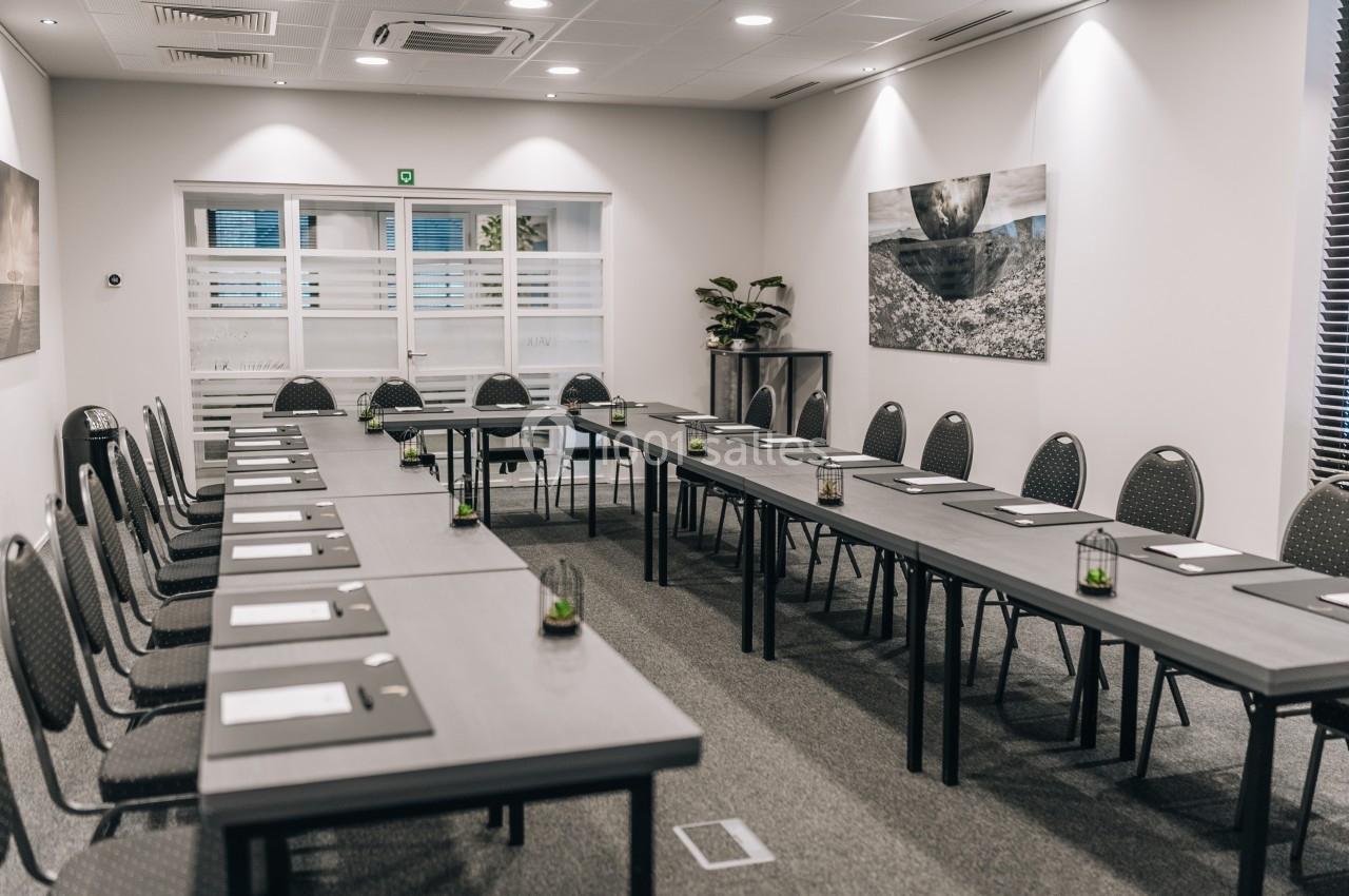 Salle de réunion moderne avec tables disposées en U, chaises, blocs-notes et décoration murale.