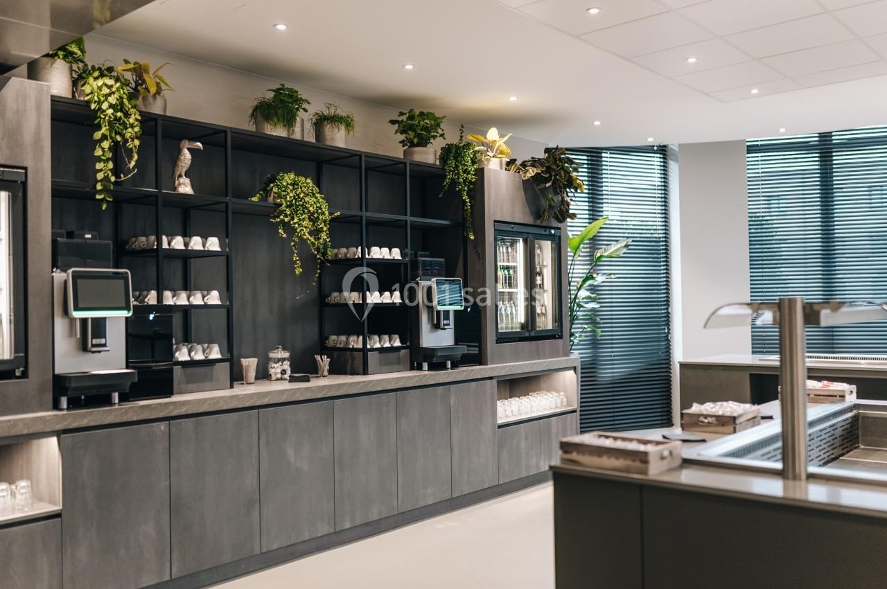 Comptoir moderne avec étagères garnies de tasses, plantes décoratives et distributeurs automatiques dans un espace lumineux.