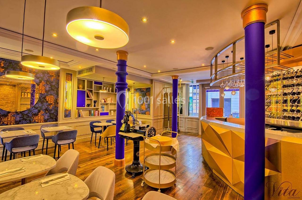 Intérieur d'un restaurant moderne avec tables en marbre, colonnes colorées, éclairage chaleureux et décor artistique.