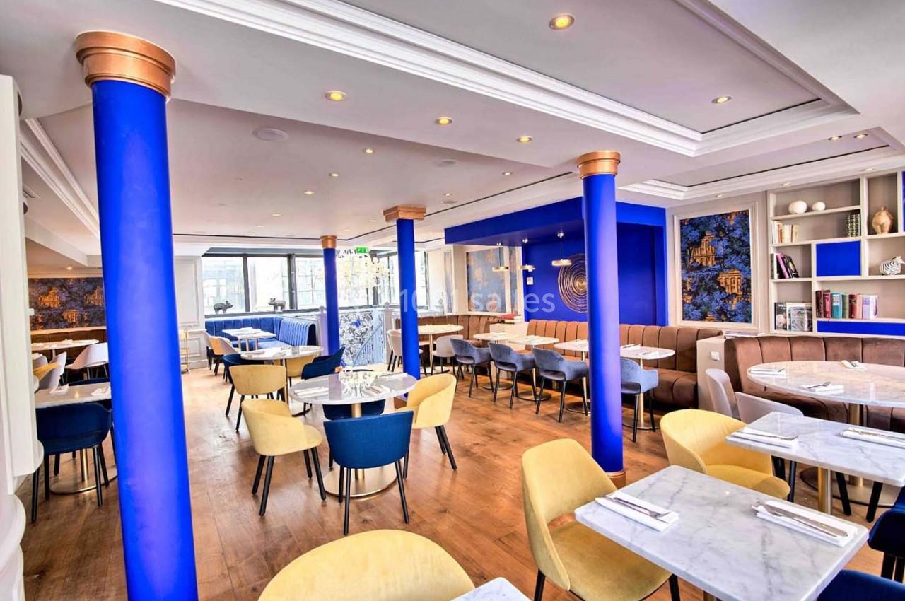 Salle de restaurant lumineuse avec des colonnes bleues, des tables en marbre, des chaises colorées et un décor moderne.